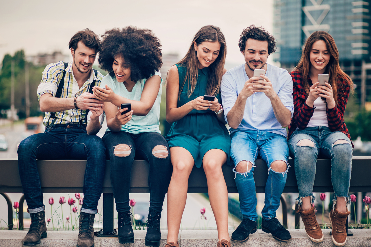 Multi-ethnic group of people sitting on an urban bridge text messaging and sharing smart phone content.